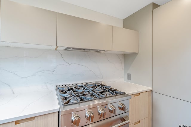 kitchen with modern cabinets, stainless steel range with gas cooktop, cream cabinetry, tasteful backsplash, and light stone counters