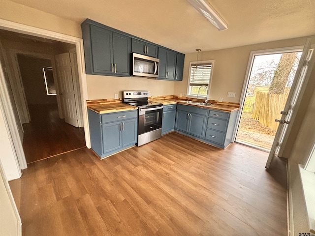 kitchen with sink, light hardwood / wood-style flooring, wooden counters, hanging light fixtures, and stainless steel appliances