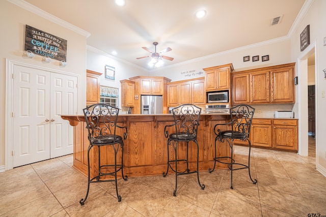 kitchen with a kitchen bar, stainless steel appliances, kitchen peninsula, ornamental molding, and ceiling fan