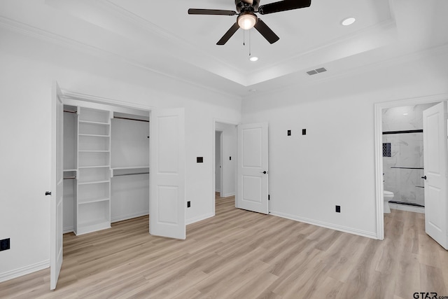 unfurnished bedroom with ensuite bath, ceiling fan, a tray ceiling, a closet, and light wood-type flooring