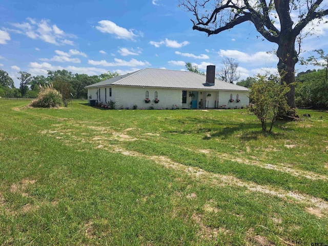 back of property featuring a yard, a chimney, and metal roof