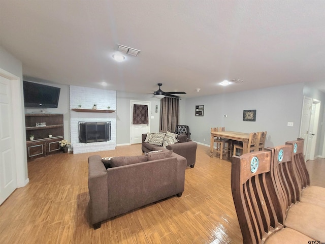 living room featuring a ceiling fan, visible vents, a brick fireplace, baseboards, and light wood-style flooring