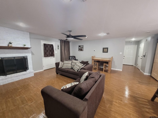 living room featuring a brick fireplace, baseboards, ceiling fan, and wood finished floors