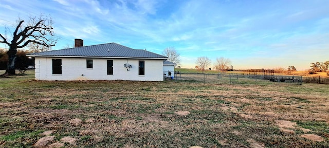 back of house featuring a chimney, metal roof, a lawn, brick siding, and fence