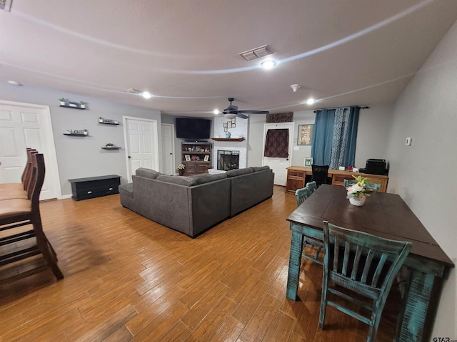 living room featuring ceiling fan, a fireplace, wood finished floors, and visible vents