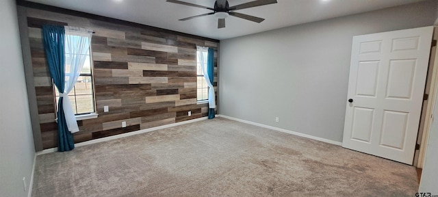 spare room featuring wooden walls, carpet floors, an accent wall, a ceiling fan, and baseboards