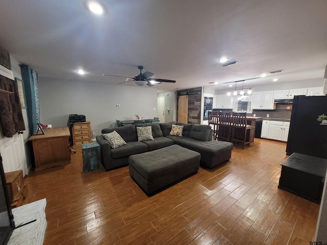 living room featuring visible vents, a barn door, ceiling fan, and wood finished floors