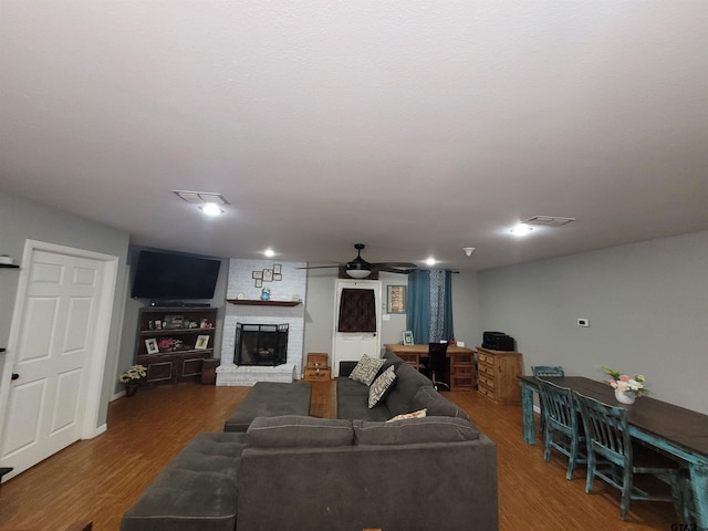 living room featuring ceiling fan, a brick fireplace, wood finished floors, and visible vents