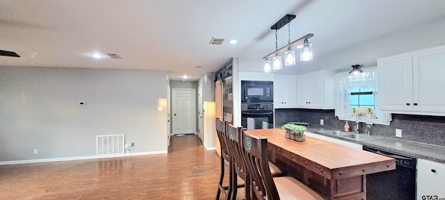 kitchen featuring a sink, decorative backsplash, black appliances, and visible vents