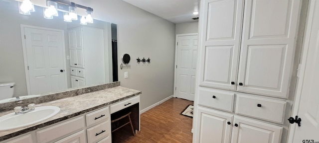 bathroom featuring toilet, baseboards, wood finished floors, and vanity