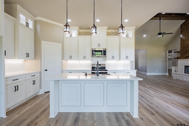 kitchen featuring ceiling fan, an island with sink, appliances with stainless steel finishes, light countertops, and backsplash