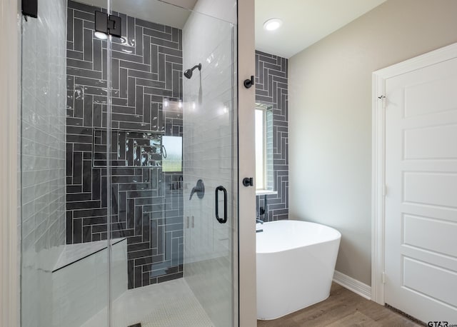 bathroom featuring a soaking tub, baseboards, a stall shower, and wood finished floors