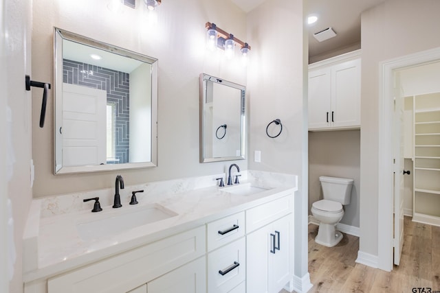 full bath with toilet, wood finished floors, double vanity, and a sink