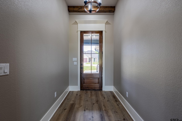 doorway to outside with dark wood-type flooring, beamed ceiling, baseboards, and a textured wall
