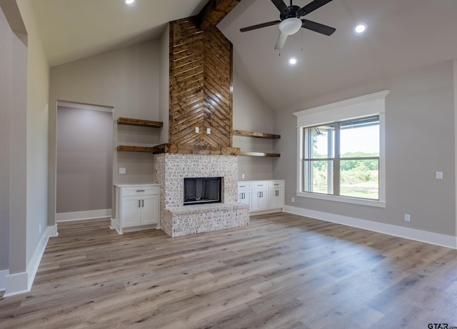 unfurnished living room with high vaulted ceiling, light wood-type flooring, a ceiling fan, a brick fireplace, and baseboards