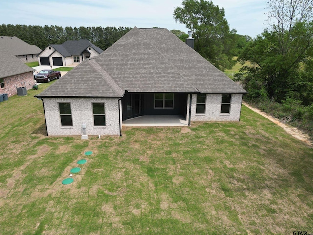 back of house featuring a yard, a shingled roof, central AC, and a patio