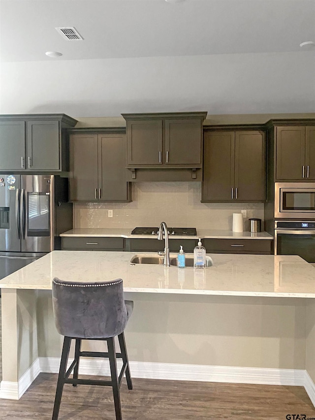 kitchen featuring a kitchen island with sink, decorative backsplash, appliances with stainless steel finishes, and light stone counters