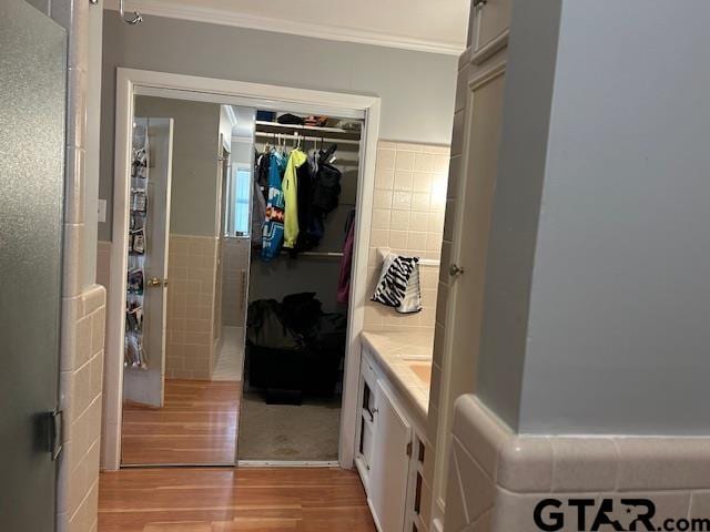 interior space featuring wainscoting, ornamental molding, wood finished floors, a walk in closet, and tile walls