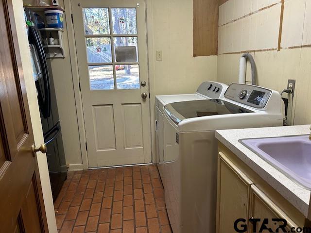 washroom featuring a sink, brick floor, cabinet space, and independent washer and dryer