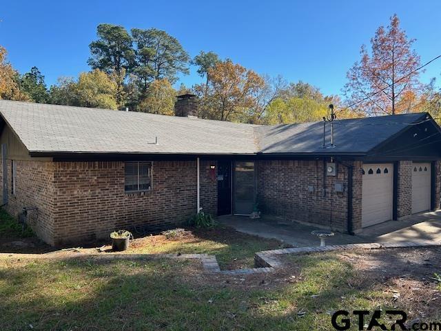 view of front of house with a garage, concrete driveway, brick siding, and a chimney