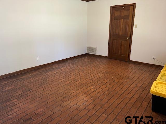 unfurnished room with brick floor, visible vents, and baseboards