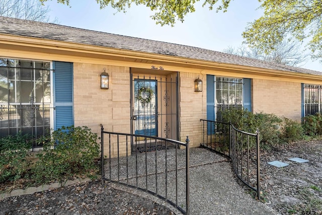 entrance to property featuring a shingled roof and brick siding