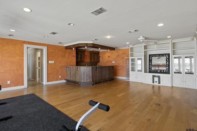 workout area featuring hardwood / wood-style flooring, ornamental molding, visible vents, and ceiling fan