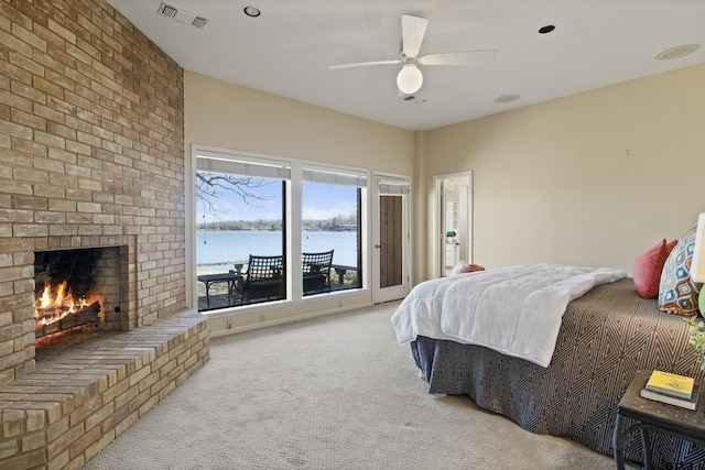 carpeted bedroom with visible vents, a water view, a brick fireplace, and a ceiling fan