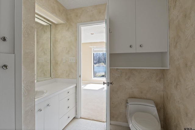 half bathroom with toilet, vanity, and wallpapered walls