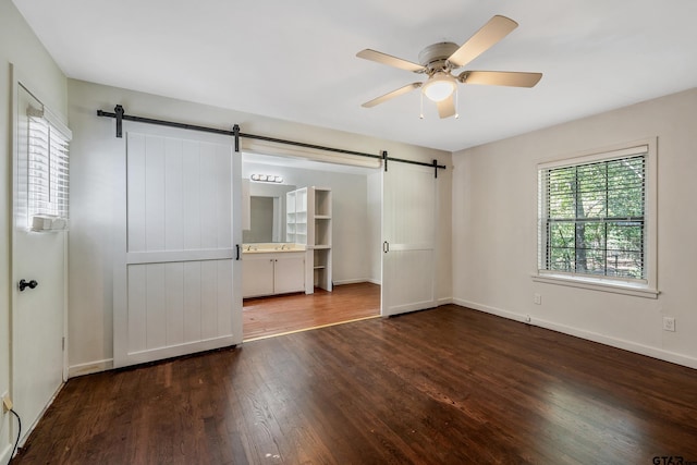 unfurnished bedroom featuring a barn door, connected bathroom, dark hardwood / wood-style floors, ceiling fan, and a closet