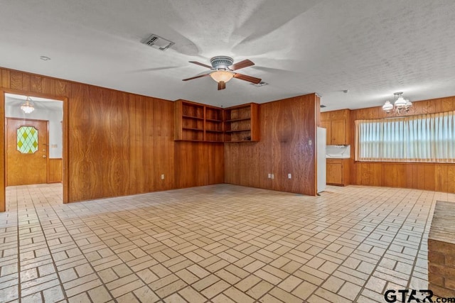 901 Dogwood St, Gilmer, TX 75644 - unfurnished living room featuring brick patterned flooring, wood walls, a chandelier, and a ceiling fan