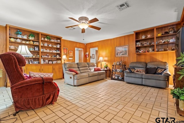 living room with wooden walls, brick floor, visible vents, and a ceiling fan