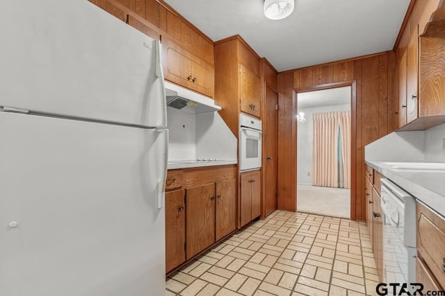 901 Dogwood St, Gilmer, TX 75644 - kitchen featuring white appliances, under cabinet range hood, light countertops, brown cabinetry, and wood walls