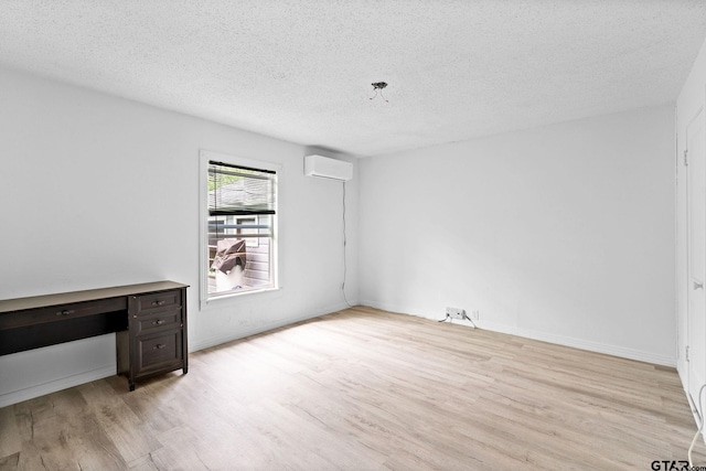 unfurnished bedroom with a wall mounted AC, light wood-type flooring, and a textured ceiling