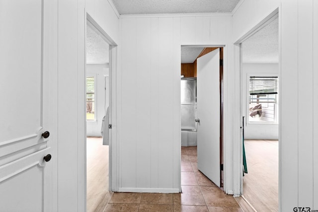 corridor featuring crown molding, a textured ceiling, tile patterned floors, and a wealth of natural light