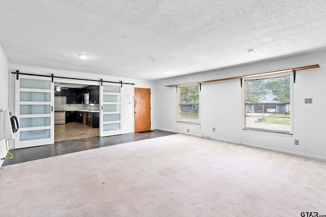 unfurnished living room with a barn door, baseboards, and a textured ceiling