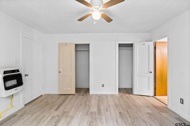 unfurnished bedroom featuring a textured ceiling, light wood-type flooring, baseboards, heating unit, and multiple closets