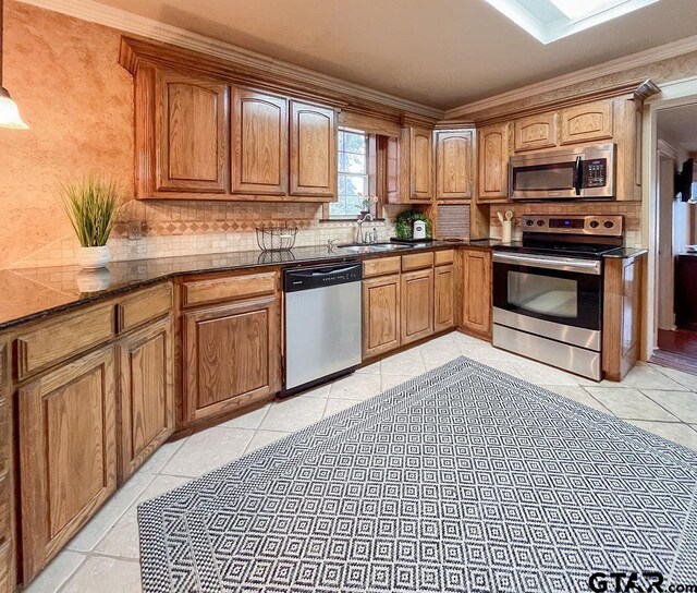 kitchen with stainless steel appliances, dark stone counters, sink, light tile patterned floors, and ornamental molding