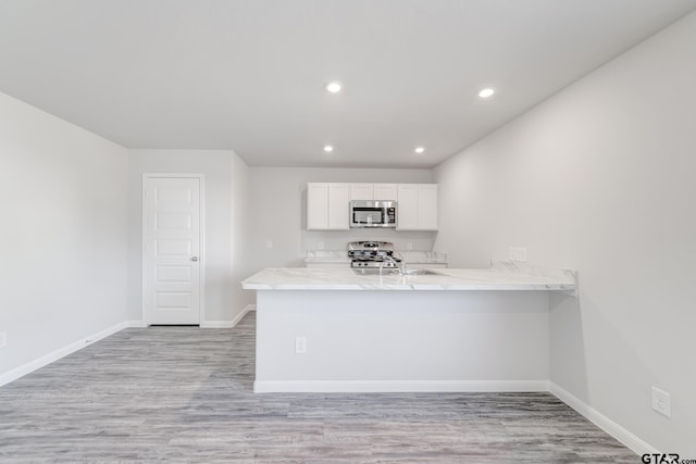 kitchen featuring light hardwood / wood-style flooring, kitchen peninsula, appliances with stainless steel finishes, and white cabinets