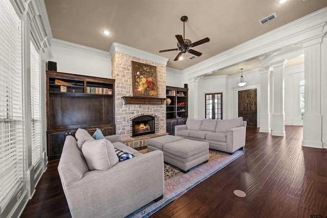 living room featuring ornate columns, dark hardwood / wood-style flooring, ornamental molding, and a stone fireplace