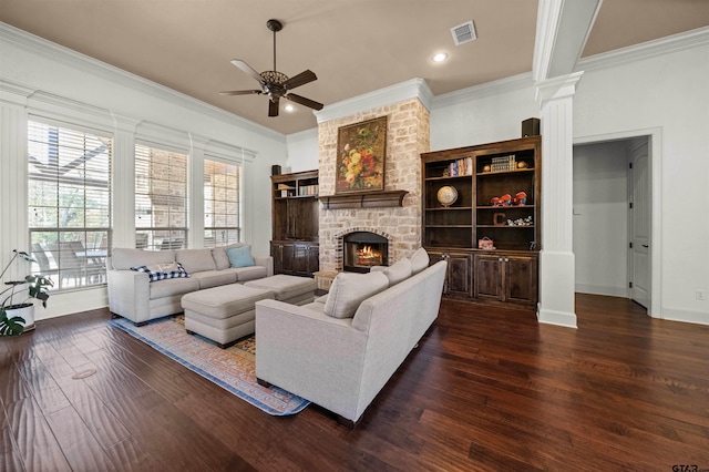 living room featuring ornate columns, a brick fireplace, dark hardwood / wood-style flooring, ceiling fan, and crown molding