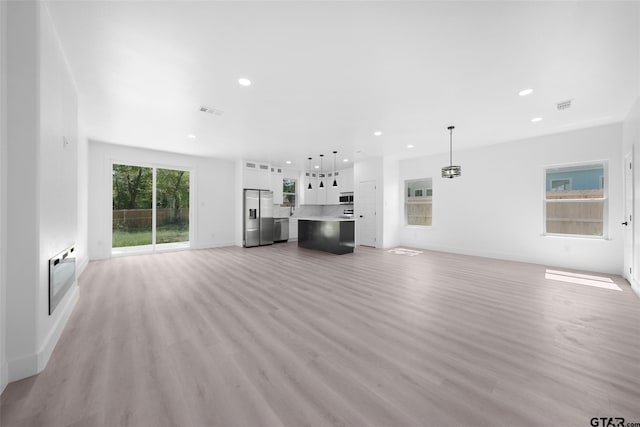 unfurnished living room with a wall unit AC, a wealth of natural light, and light hardwood / wood-style floors