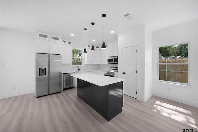 kitchen with white cabinets, appliances with stainless steel finishes, a healthy amount of sunlight, and a center island