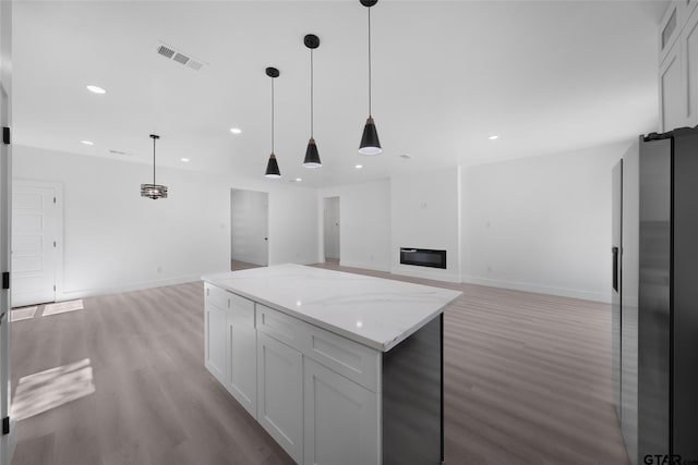 kitchen featuring light stone countertops, white cabinetry, pendant lighting, and light hardwood / wood-style flooring