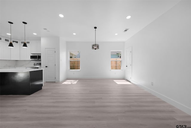 interior space featuring white cabinetry, appliances with stainless steel finishes, decorative light fixtures, and light wood-type flooring