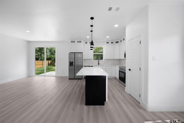 kitchen featuring a center island, stainless steel appliances, white cabinetry, hanging light fixtures, and light hardwood / wood-style flooring