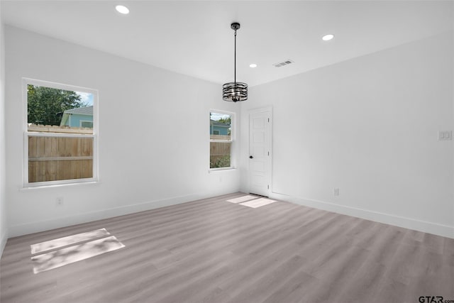 spare room featuring light wood-type flooring, a wealth of natural light, and an inviting chandelier