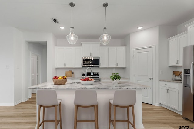 kitchen featuring pendant lighting, appliances with stainless steel finishes, an island with sink, and white cabinets