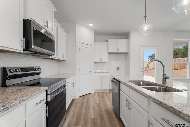 kitchen with sink, hanging light fixtures, stainless steel appliances, light stone countertops, and white cabinets