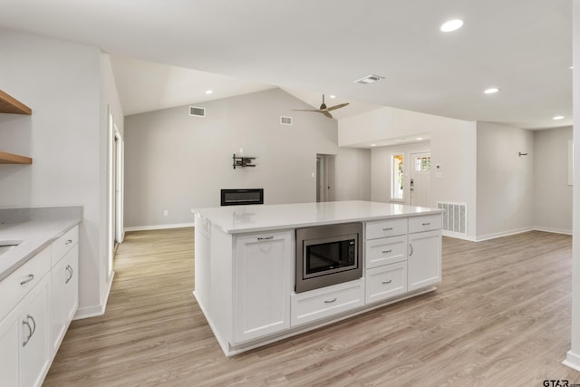 kitchen with light hardwood / wood-style floors, ceiling fan, a kitchen island, stainless steel microwave, and white cabinets